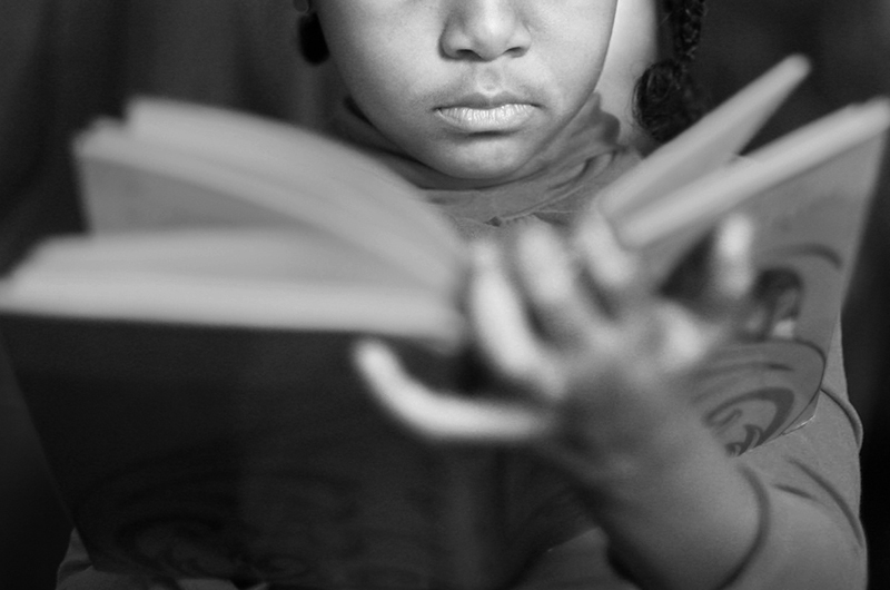Cute little Afro-American girl in casual clothes reading a book.